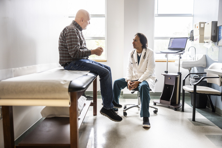 Photo shows doctor and senior man discussing treatment in exam room/Getty Images