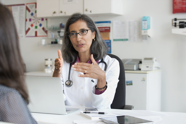 Photo shows a doctor speaking to her patient in a medical facility/Getty Images