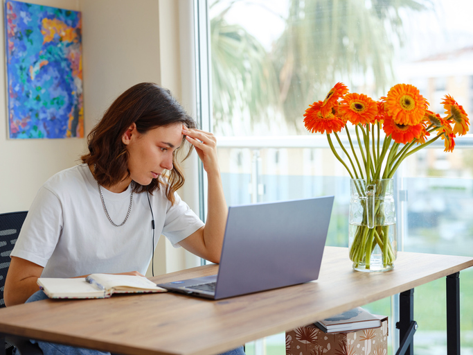 Photo shows woman holding forehead while working from home/Getty Images