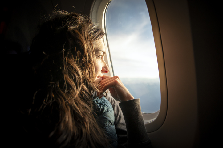 Photo shows a woman looking out of an airplane window at sunrise/Getty Images