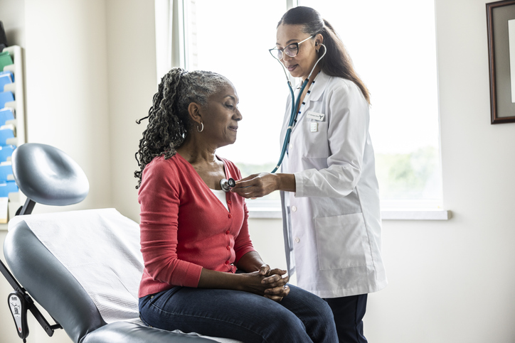 Female doctor listening to senior woman's heart in exam room/Getty Images