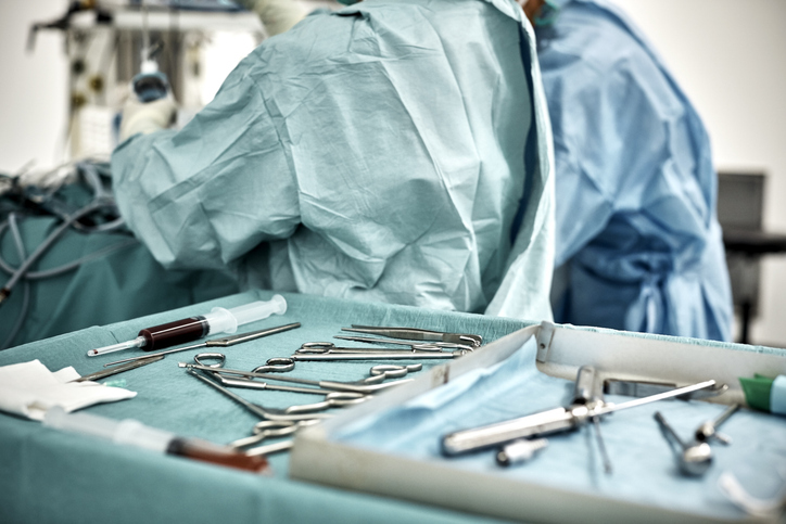 Photo shows a close-up of surgical equipment in tray on table against surgeons in operating room/Getty Images