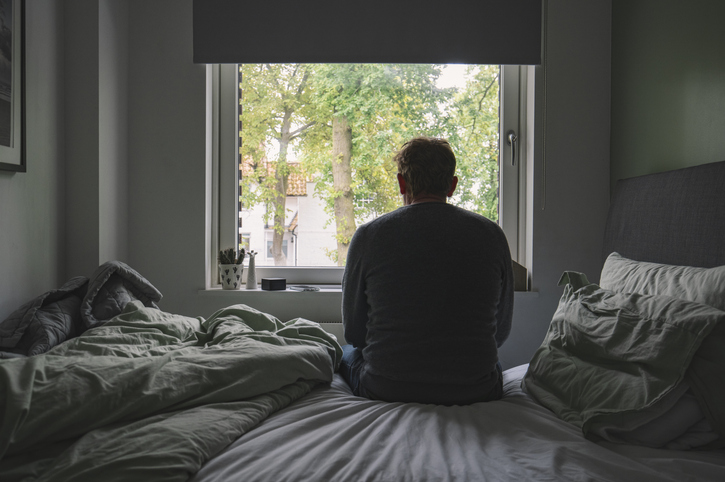 Photo shows a man sitting on a bed and looking out the window/Getty Images